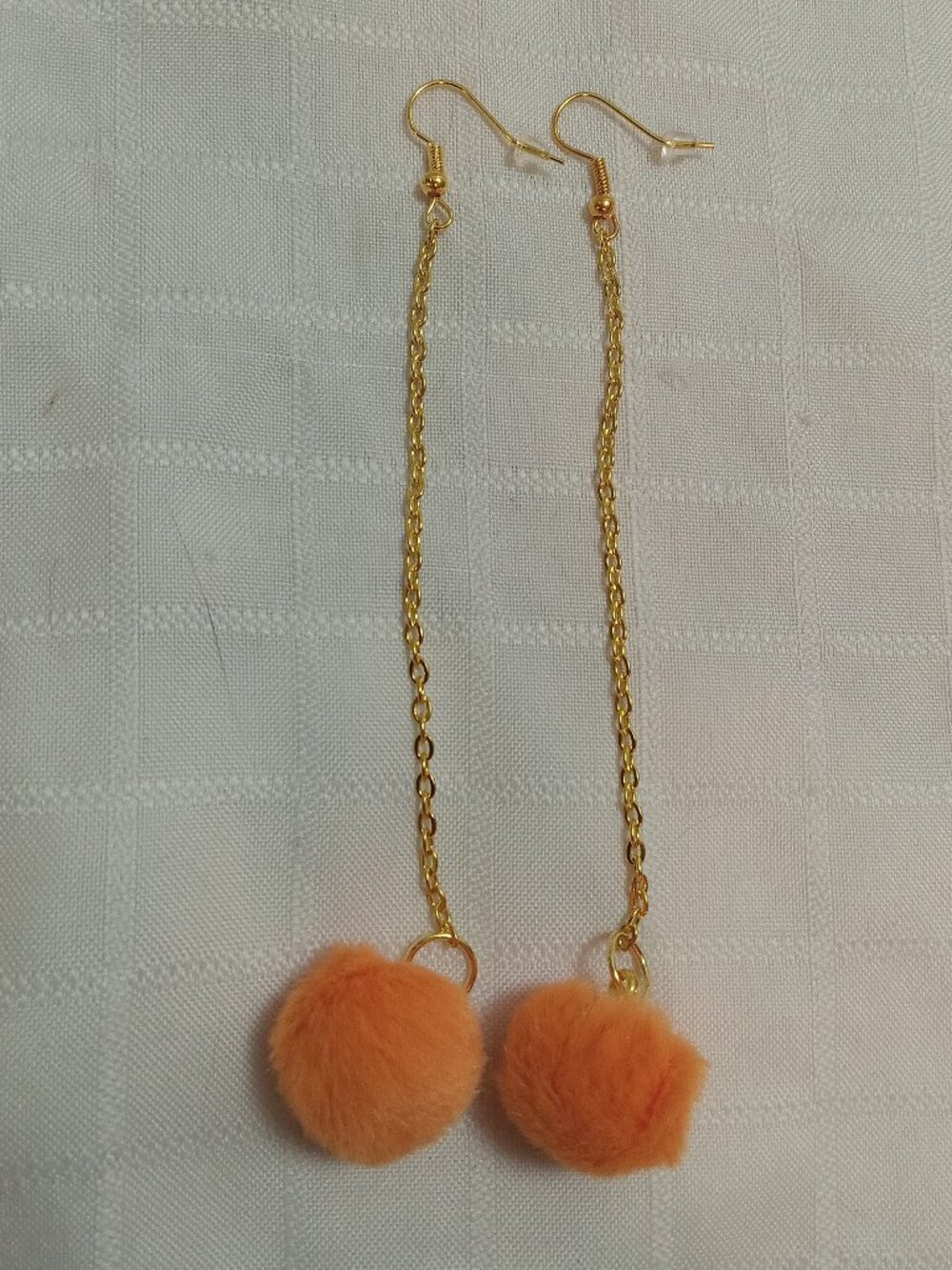 Handmade earrings with small pom-poms and gold-colored accent hooks and chains